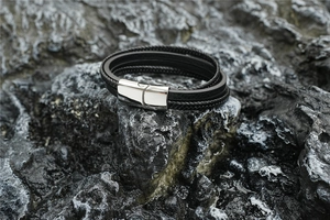 Détail d'un bracelet multicouche en cuir noir tressé avec un fermoir magnétique en métal