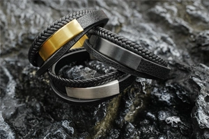Close-up of triple-layered black leather bracelets with gold, black, and silver metal bars