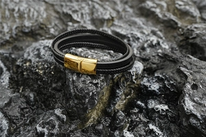 Détail d'un bracelet multicouche en cuir noir avec un fermoir magnétique doré sur basalte