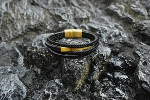 Detail of multi-layer leather braid bracelet with gold magnetic clasp on dark rock