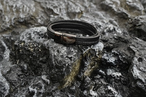 Détail d'un bracelet multicouche en cuir tressé noir avec fermoir magnétique sur roche