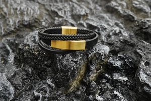 Close-up of triple-layer black leather braid bracelet with a gold magnetic clasp on a rock