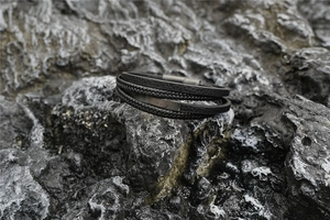 Detail of layered black leather braided bracelet on dark rock surface with metal clasp