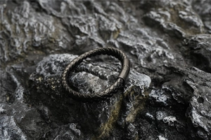 Gros plan du bracelet en cuir tressé noir avec fermoir en métal mat sur roche naturelle