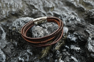 Macro detail of men's multi-layer braided leather bracelet with silver magnetic clasp