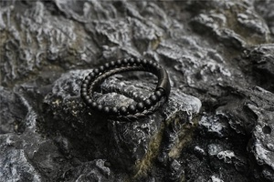 Détail d'un bracelet double épaisseur pour homme avec perles mates et cuir tressé sur roche