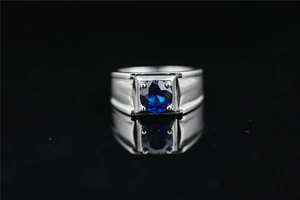 Primer plano de anillo plateado para hombre con gema azul sobre fondo negro reflectante