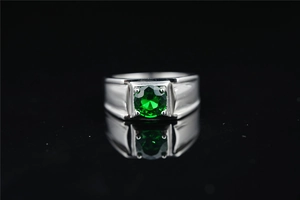 Vista macro de un anillo ancho plateado para hombre con una piedra preciosa verde redonda engastada