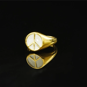 Minimalist gold ring with white enamel peace symbol on a black reflective background