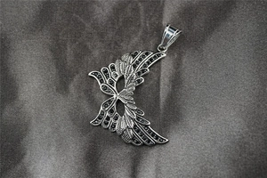 Macro detail of silver wing pendant with black pave stones on dark satin fabric background