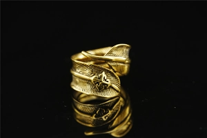 Detailed close-up of retro golden feather ring with a carved cross symbol on black surface