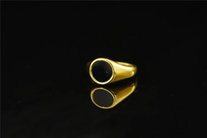 Macro shot of gold-plated signet ring with black circular enamel inlay on reflective surface