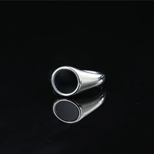 Minimalist silver metal ring with a round black enamel inlay on a reflective surface