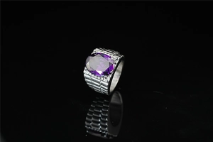 Macro detail of oval purple gemstone ring with silver-tone textured band on black surface