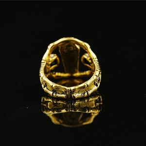 Gothic gold skeleton ring with coffin detail shown on a sleek black reflective background