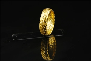 Close-up of golden tire-textured ring with relief wheat pattern on black mirror background