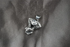 Detailed view of silver stainless steel V-twin motorcycle engine pendant on grey fabric