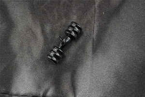 Macro shot of a black plated dumbbell stud earring on a dark textured fabric backdrop