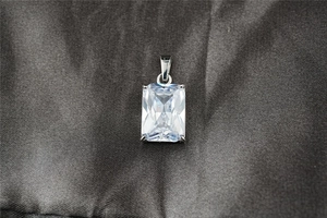 Dettaglio del ciondolo rettangolare in moissanite su elegante tessuto di seta grigio