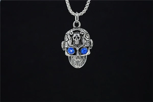 Détail du pendentif crâne gothique argenté avec yeux en strass bleus et gravures