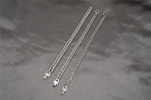 Detailed view of three different widths of polished Cuban link bracelets on grey silk