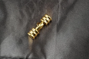 Macro shot of gold dumbbell pendant with textured weights on silk background