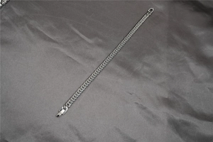 Detailed view of silver Cuban link bracelet with flat clasp on grey satin fabric