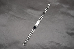 Detailed macro view of a polished stainless steel Cuban link bracelet with a blank ID tag