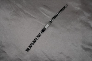 Macro detail of black Cuban link bracelet with engraved wave pattern on metal ID tag