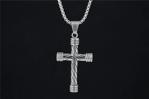 Détail du pendentif croix torsadée vintage sur une chaîne à mailles carrées en gros plan