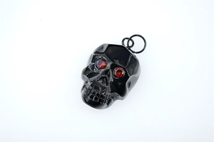 Gros plan d'un pendentif crâne en métal noir avec des yeux en cristal rouge et fini poli