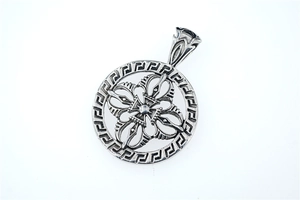 Macro detail of vintage stainless steel round pendant with vajra cross and Greek key pattern