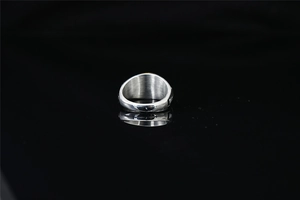 Gros plan d'une bague chevalière en argent poli sur une surface réfléchissante noire