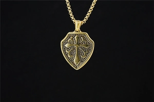 Detail of golden cross shield pendant with textured metal grains and box chain