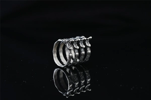 Detailed close-up of punk style silver-toned steel rib bone ring on reflective black surface