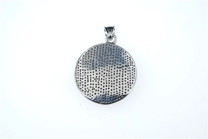 Détail macro d'un pendentif rond en titane avec design alvéolé et finition argentée