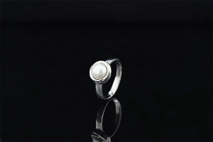 Macro shot of a minimalist silver ring featuring a single round pearl on a dark surface