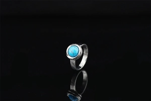Detailed close-up of a silver ring with a turquoise gemstone on a black reflective surface
