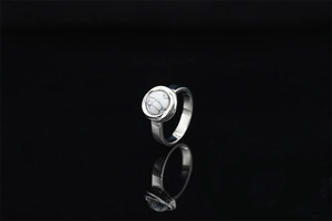 Macro shot of silver metal ring with a round white marble gemstone on black background
