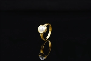 Close-up of golden metal ring featuring a round white pearl on a reflective black base