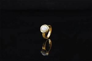 Detail of a minimalist gold ring featuring a round white turquoise stone on a black mirror