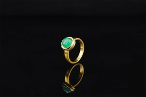 Macro shot of a gold-plated ring featuring a round green gemstone on black mirror background