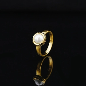 Minimalist gold-polished ring with round white pearl inlay on a black background
