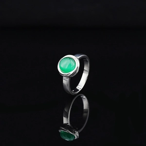 Minimalist silver ring with green round gemstone on reflective black background