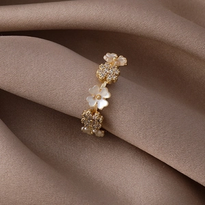 Elegant gold flower ring with white shell petals and zircon crystals on brown satin