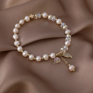 Close-up of freshwater pearl and crystal bracelet with gold wing and clover charms