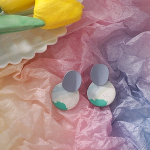 Macro shot of abstract clay earrings with blue and green textures on colorful paper