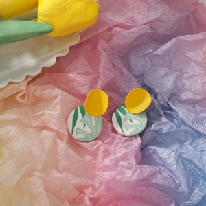 Detail of handmade clay earrings with yellow semicircles and green leaf vein patterns