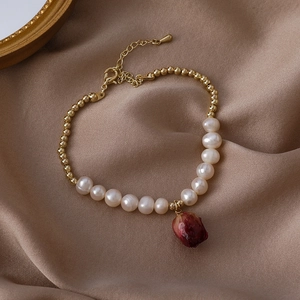 Close-up of pearl necklace with gold beads and a natural red dried rose bud pendant