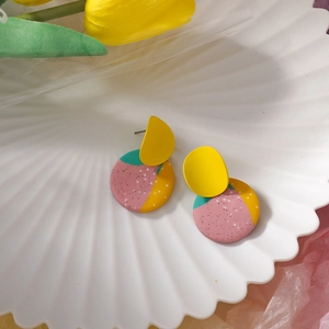 Handmade geometric clay earrings with colorful patterns on a white shell tray